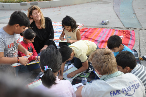Kinder sitzen mit Betreuerin auf Picknickdecken und schreiben etwas 
